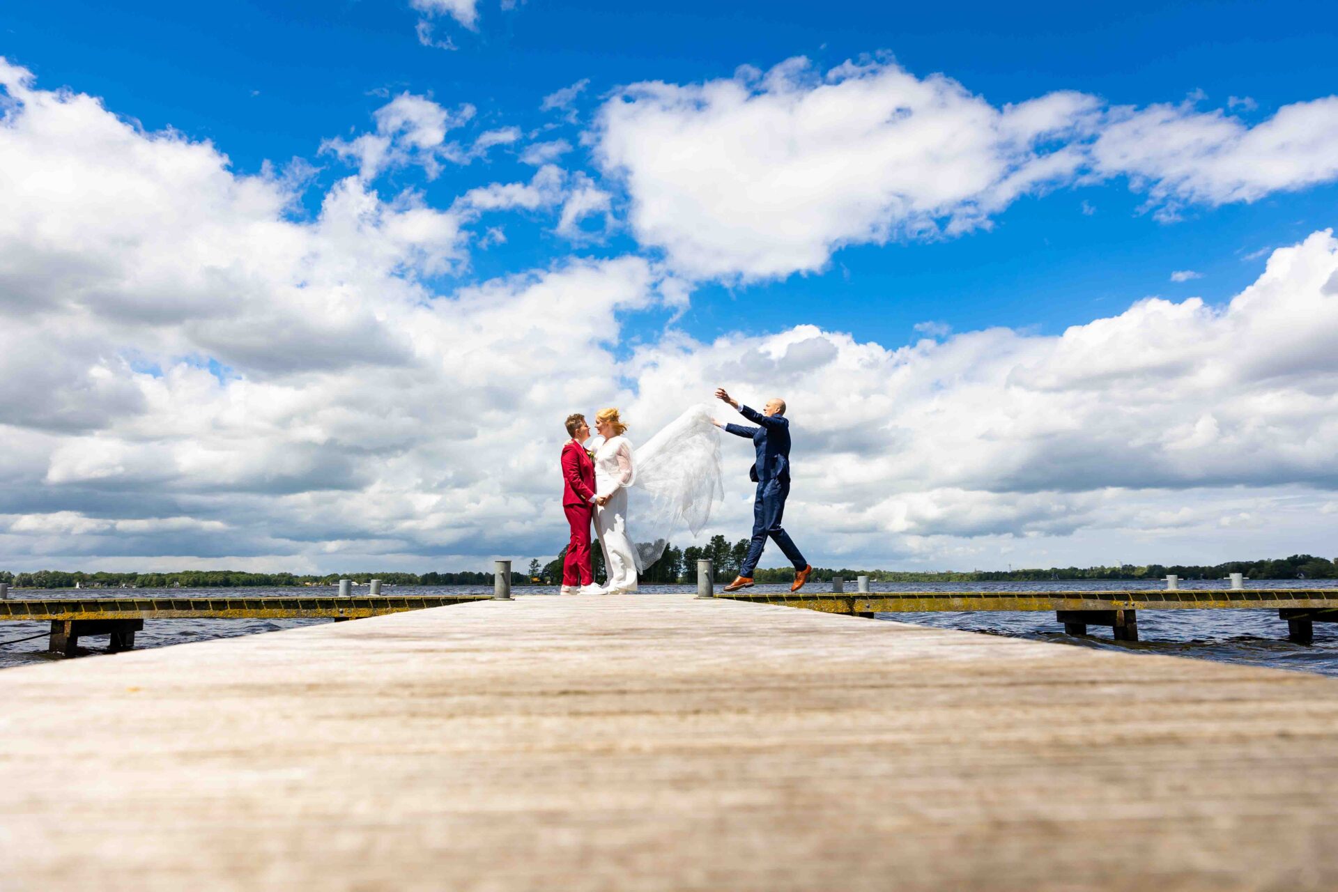 Reportage bruidspaar op de steiger bij Rietland waarbij de broer van de bruid haar jurk in de lucht gooit - Trouwfotograaf Bruidsfotograaf Groningen